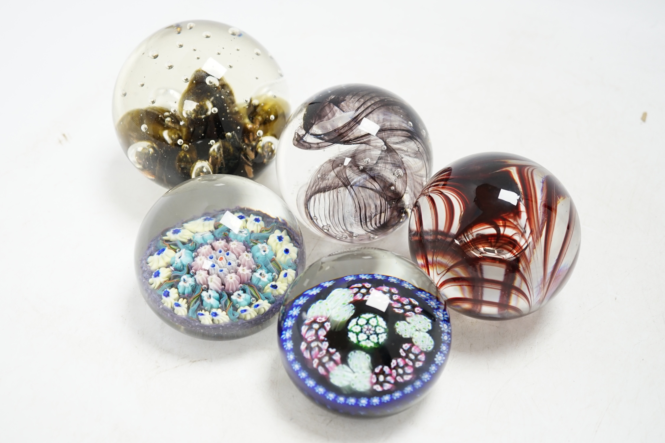 Five glass paperweights to include a Langham Glass House example and two millefiori examples, largest 9cm diameter., Condition - four good, one with impact damage